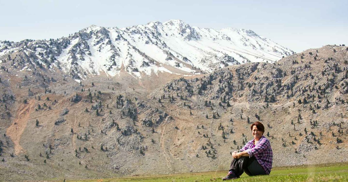 A snow-capped ridge of the western Taurus mountains above Antalya, with Yasemin Konuralp sitting on the spring turf at the foot of the slope.