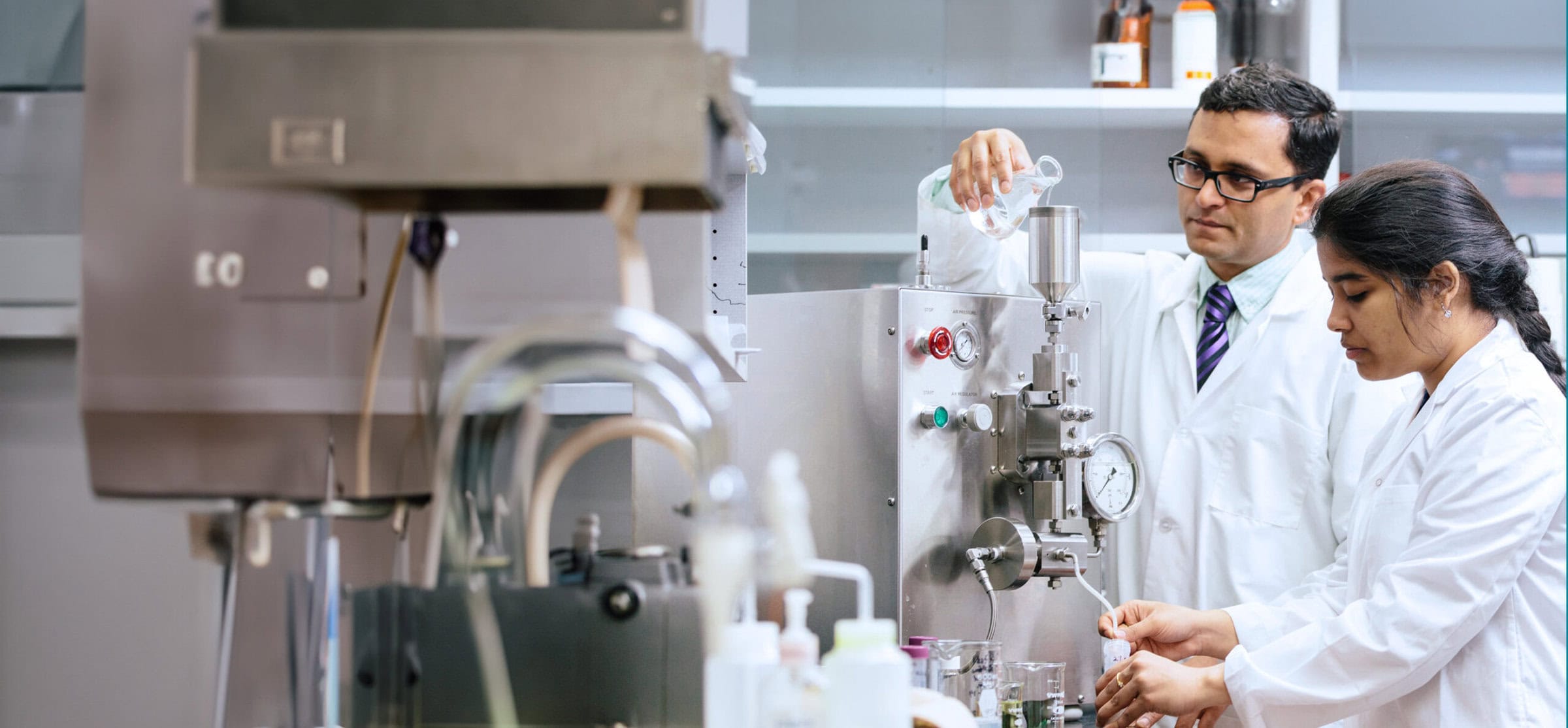 Two scientists in lab coats working with industrial lab equipment in a laboratory setting.