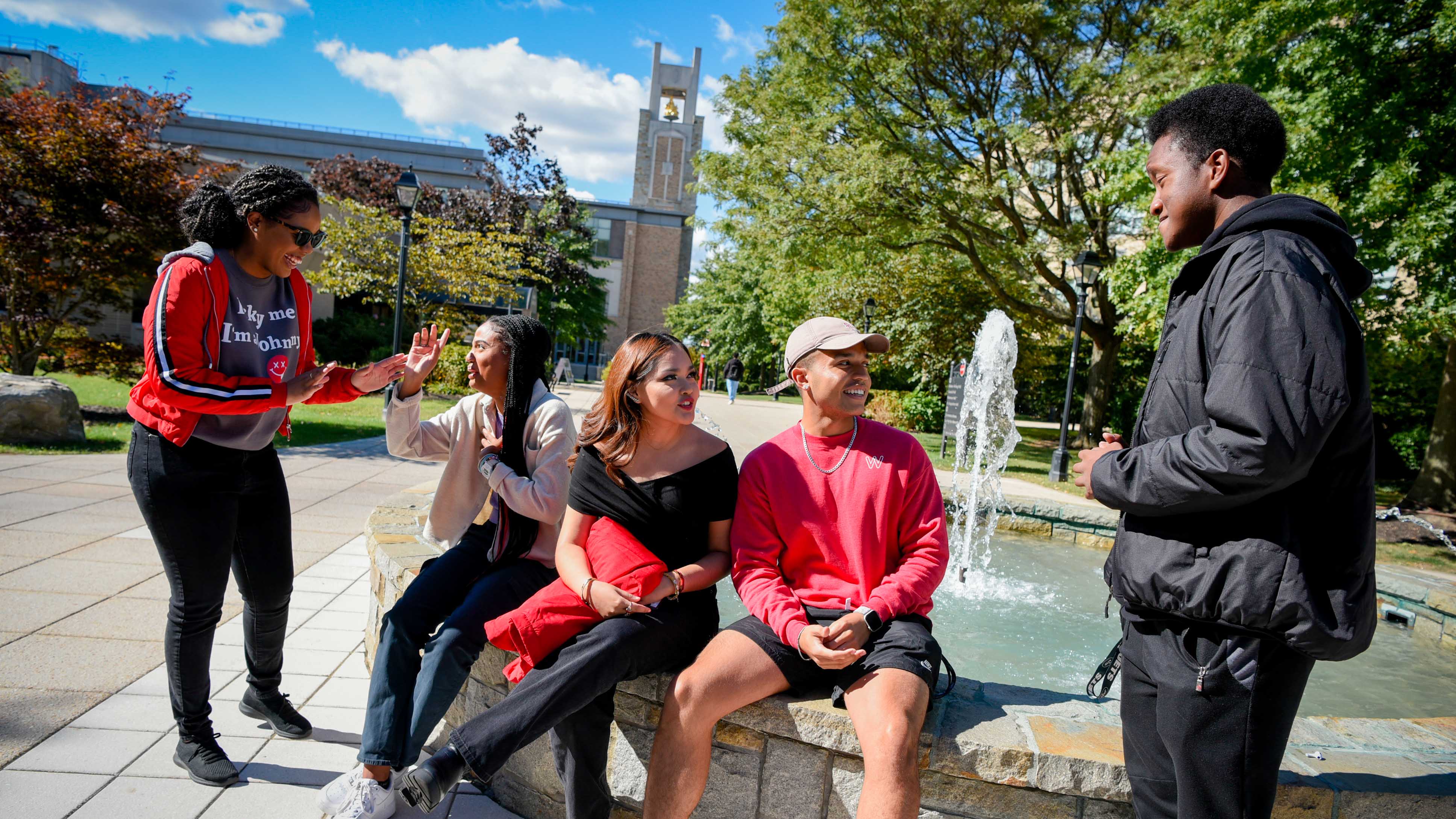 A Group of 5 students hanging outside next to a water fountain talking and laughing