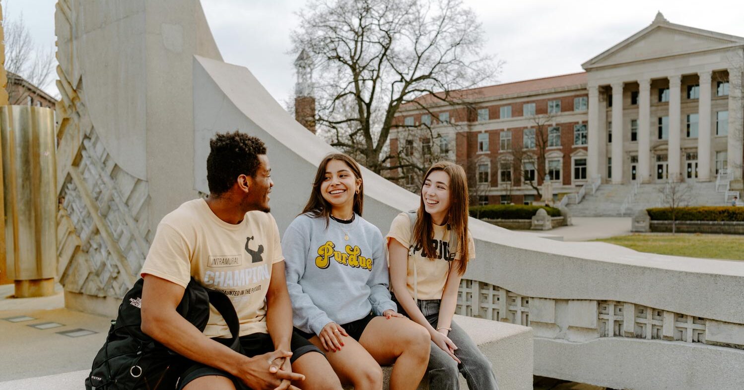 Purdue University students laughing and sitting on the Engineering Fountain at the main campus of Purdue University in West Lafayette, Indiana.