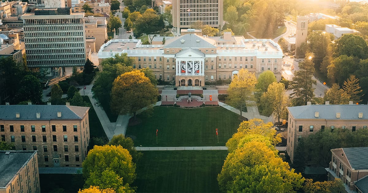An early fall aerial photo of Bascom Hall and Bascom Hill with late afternoon sun rays visible. The grass is green and some trees are turning yellow.